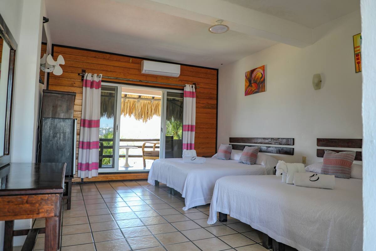 Habitación de hotel con dos camas, techo de madera, un ventanal con cortinas, un ventilador y vistas al exterior.
