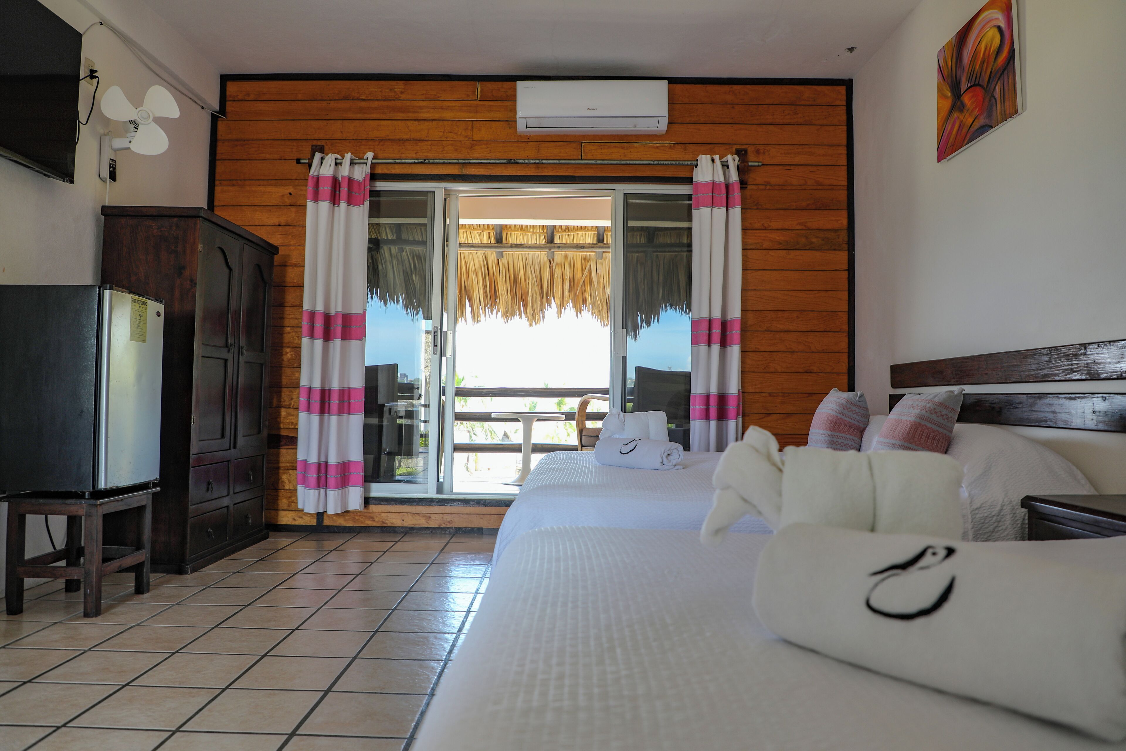 Quarto de hotel com cama, escrivaninha, armário e varanda com cortinas.