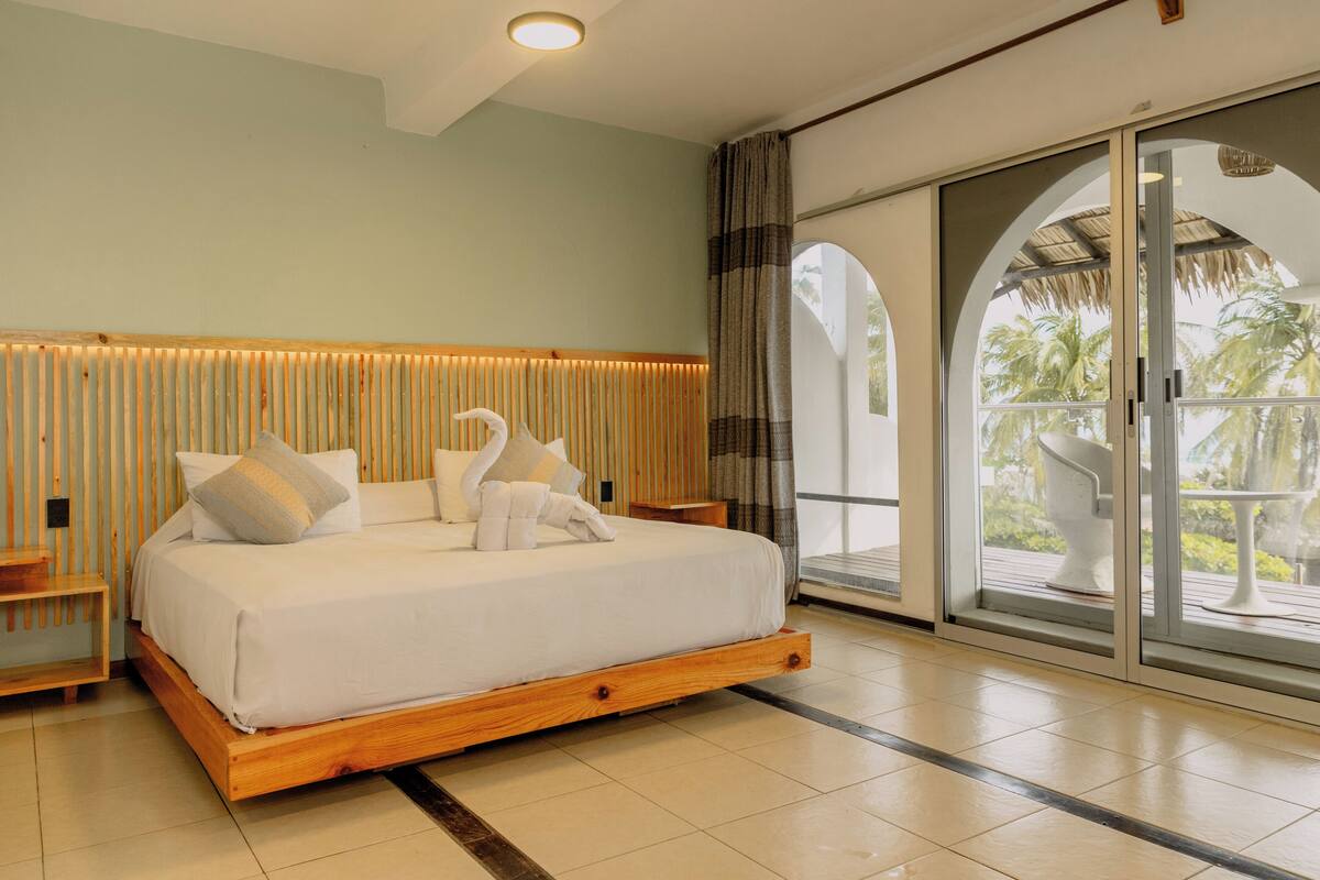 Un dormitorio amplio con una cama grande, cabecera de madera y vistas a palmeras a través de un ventanal corredero.
