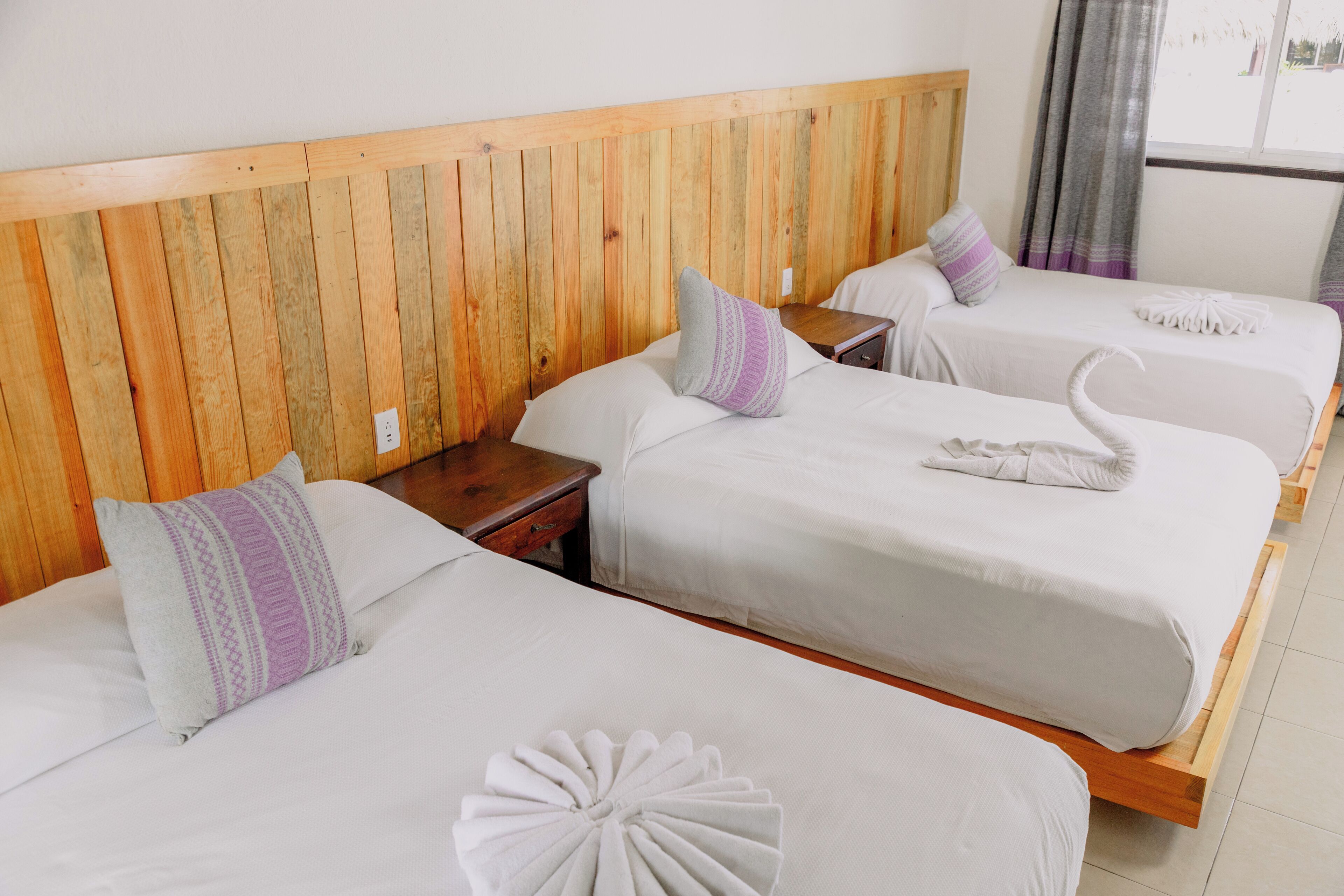 A hotel room with three beds, wooden headboard, white bedding, and a small wooden nightstand.