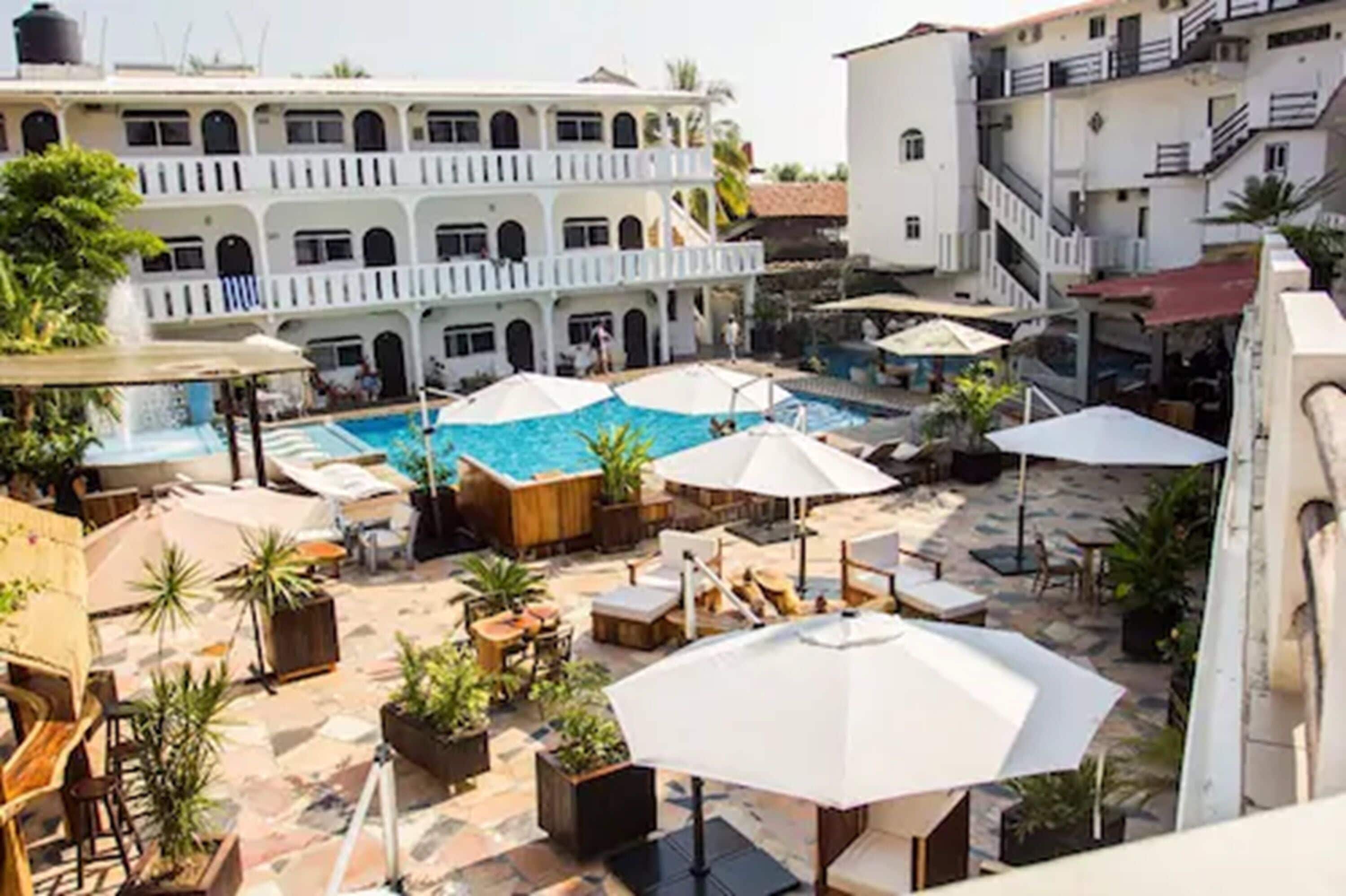 A rooftop pool area with lounge chairs, umbrellas, and potted plants.