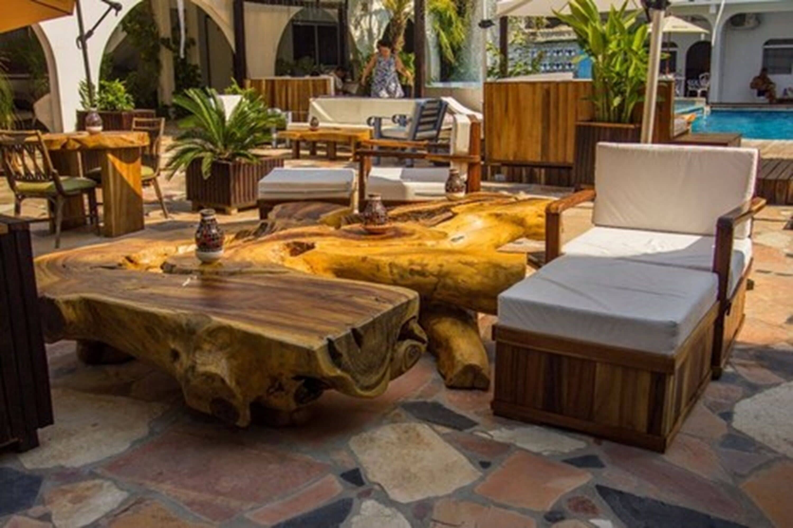 A poolside area with wooden furniture, a large log table, and a pool in the background.