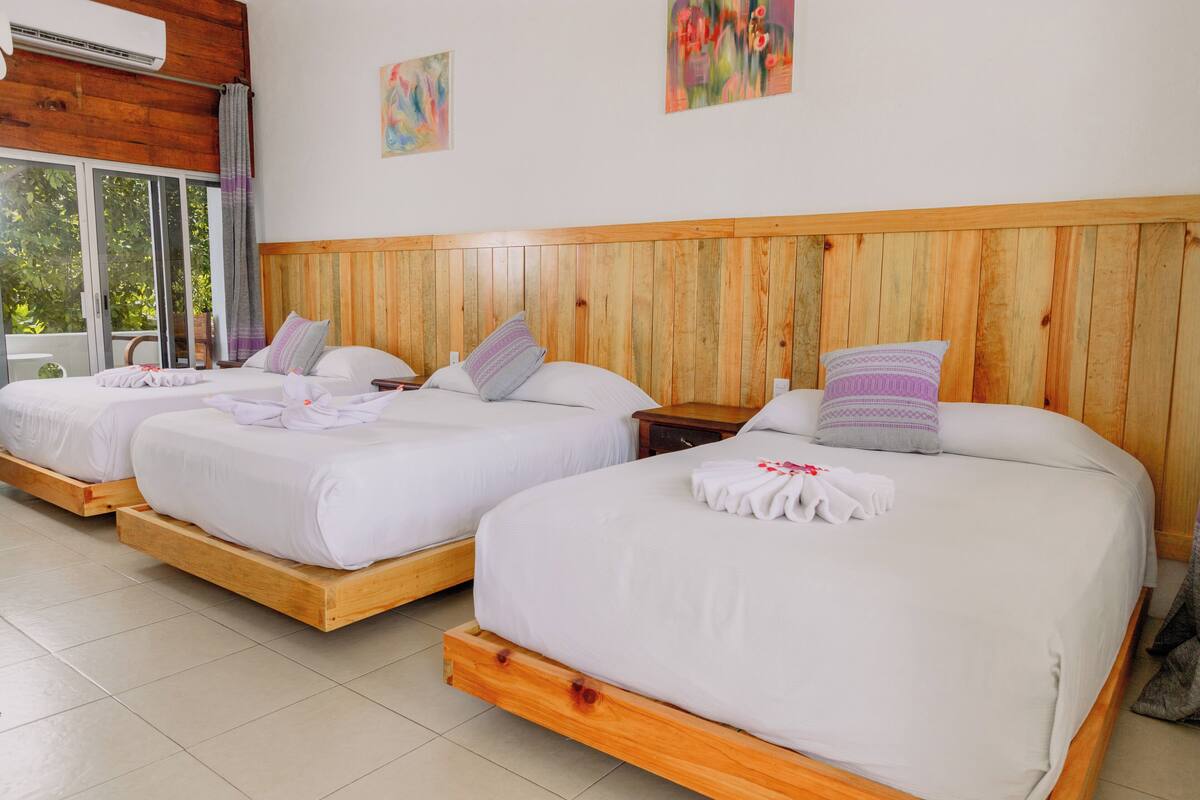Una habitación de hotel con tres camas de madera, cada una con ropa blanca y almohadas decorativas.