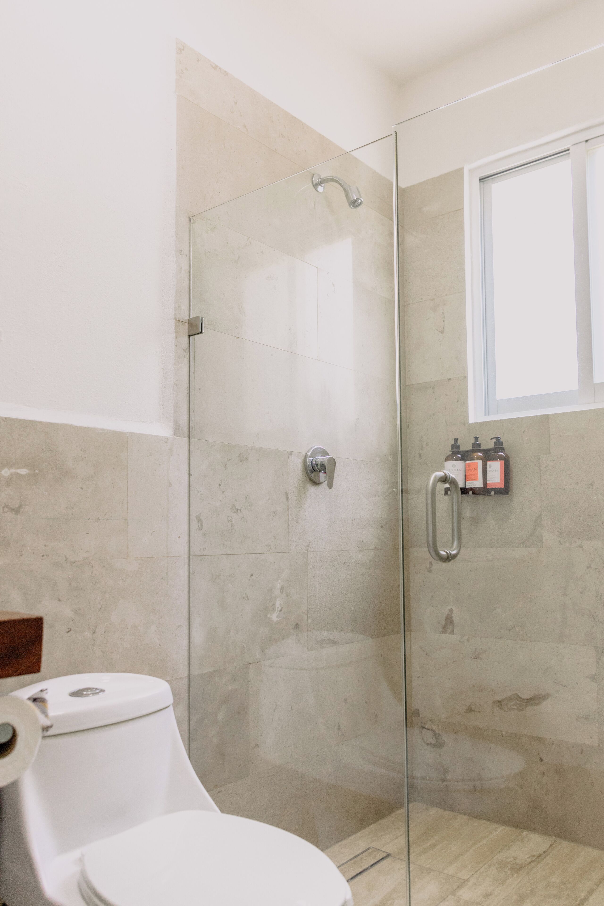 A modern bathroom with a glass shower enclosure, a toilet, and a window.