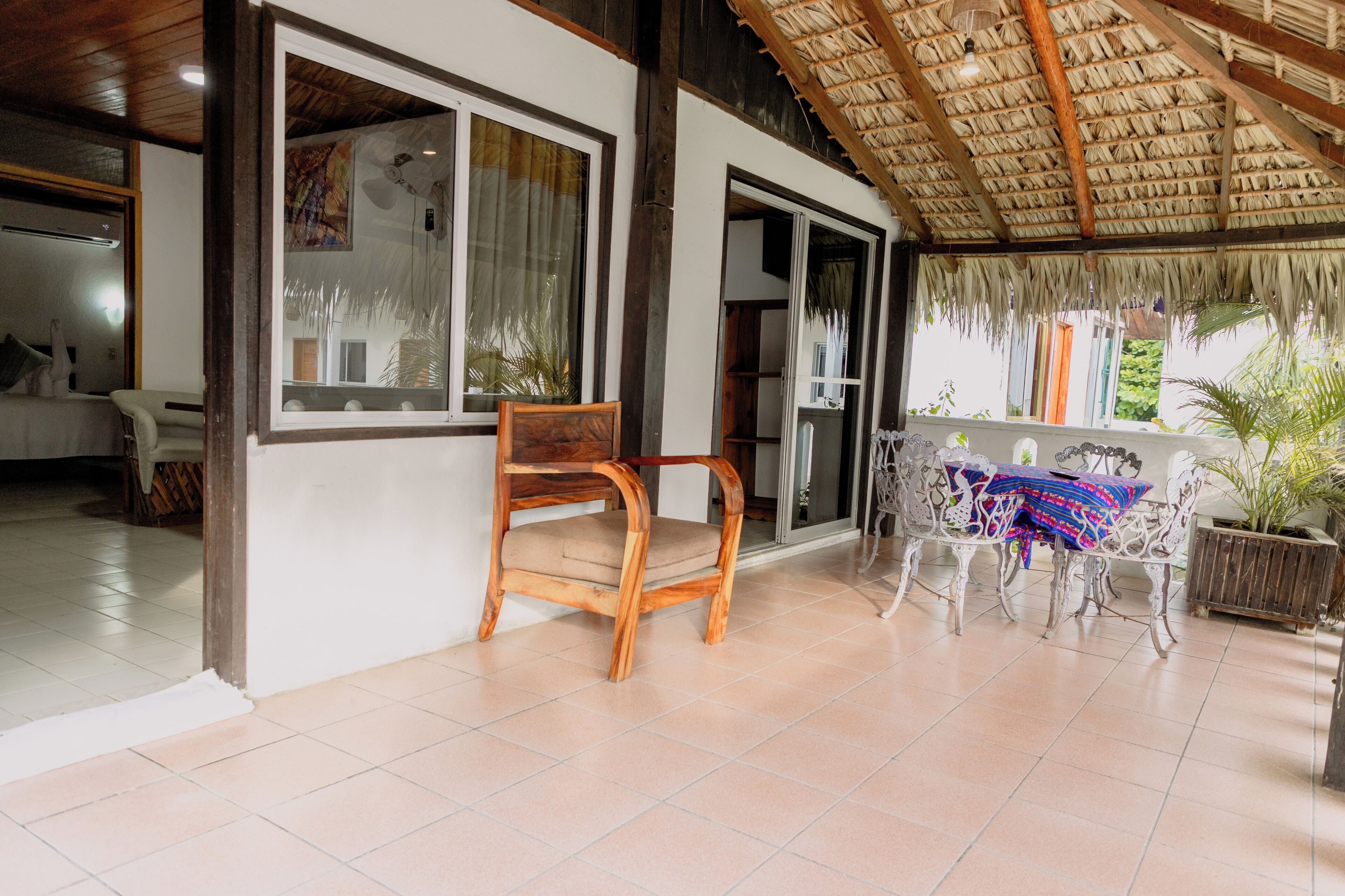 A room with a wooden chair, a table with a colorful cloth, and a thatched roof.