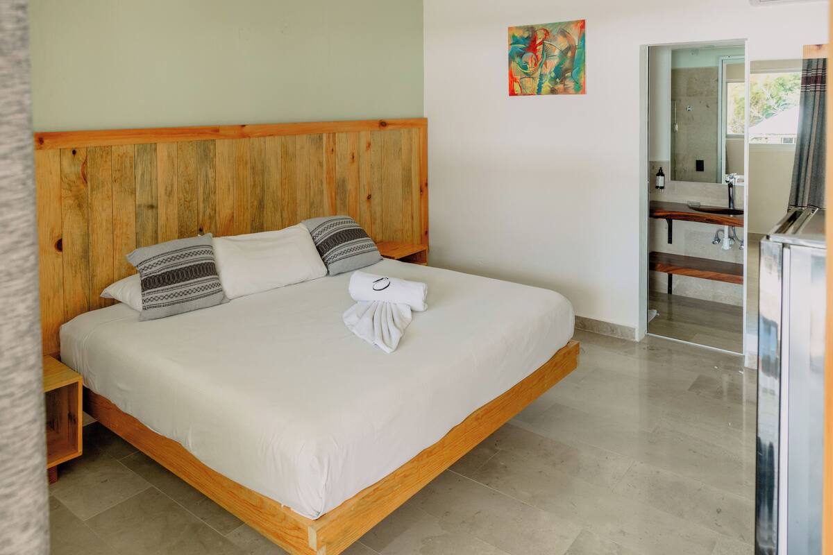 Una cama con cabecera de madera, colchón blanco y almohadas estampadas.