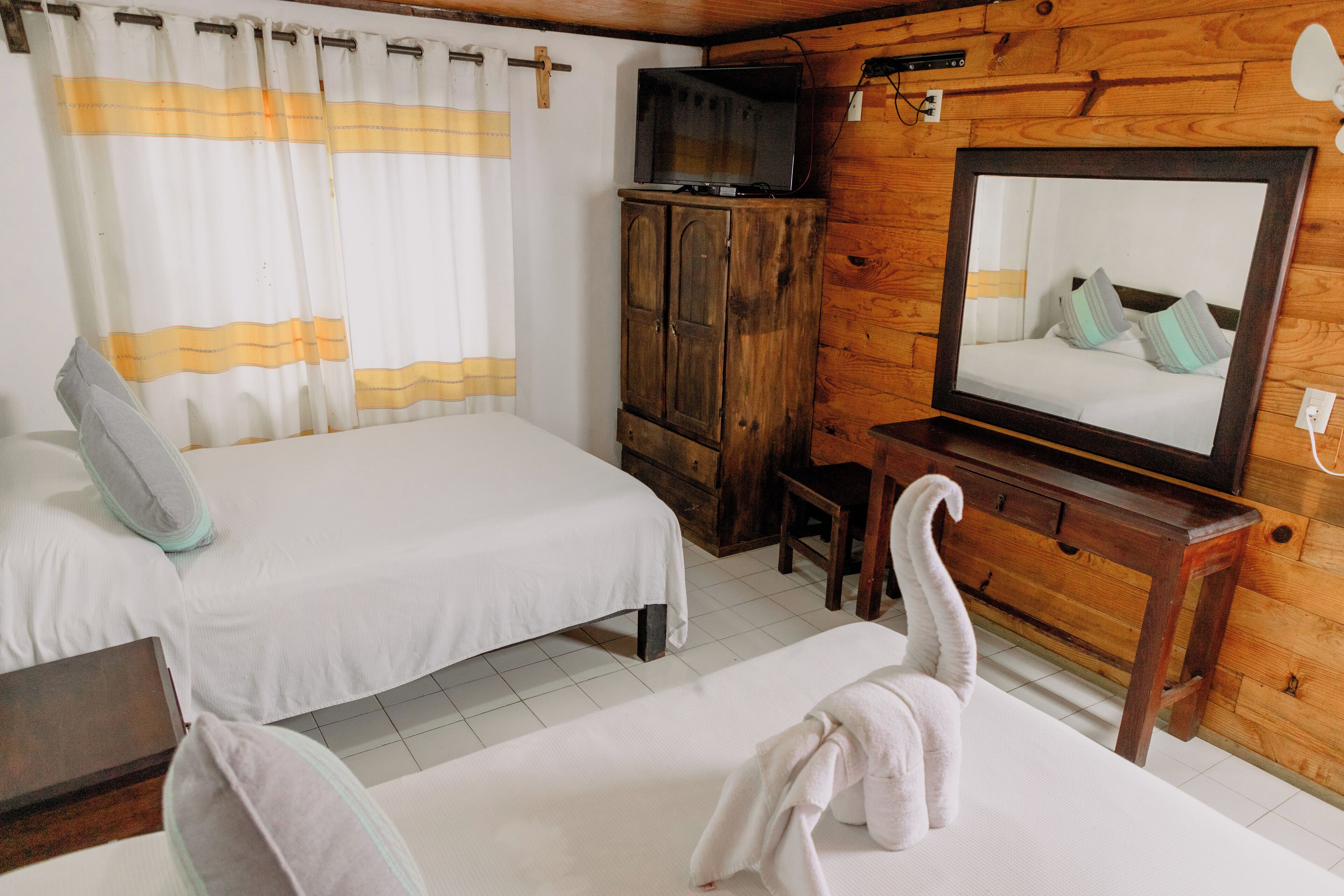 Una habitación con dos camas, armarios de madera, televisor y espejo.