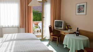 A hotel room with two beds, a desk with a television, a small table with drinks, and a view of the outdoors.