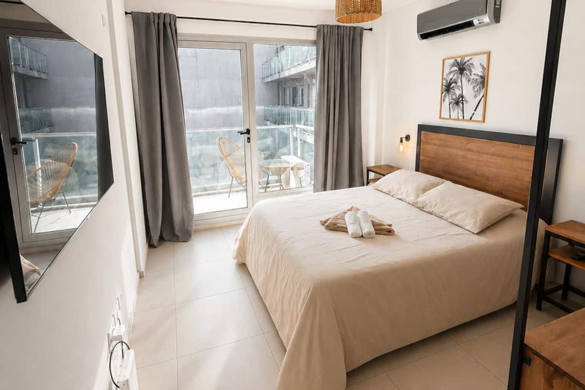 A bedroom with a bed, a window, a ceiling fan, and a view of a balcony.