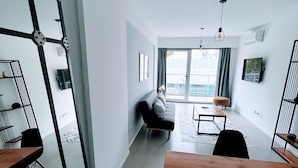 Ett modernt vardagsrum med en soffa, ett soffbord och ett matbord. Det finns ett stort fönster med utsikt över omgivningen.