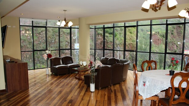 Amplia sala de estar con piso de madera, sofás de cuero, una mesa de comedor con sillas y ventanas grandes que ofrecen vista a la vegetación.