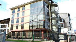 Un edificio de varios pisos con fachada de vidrio, balcones y entrada protegida por una reja.