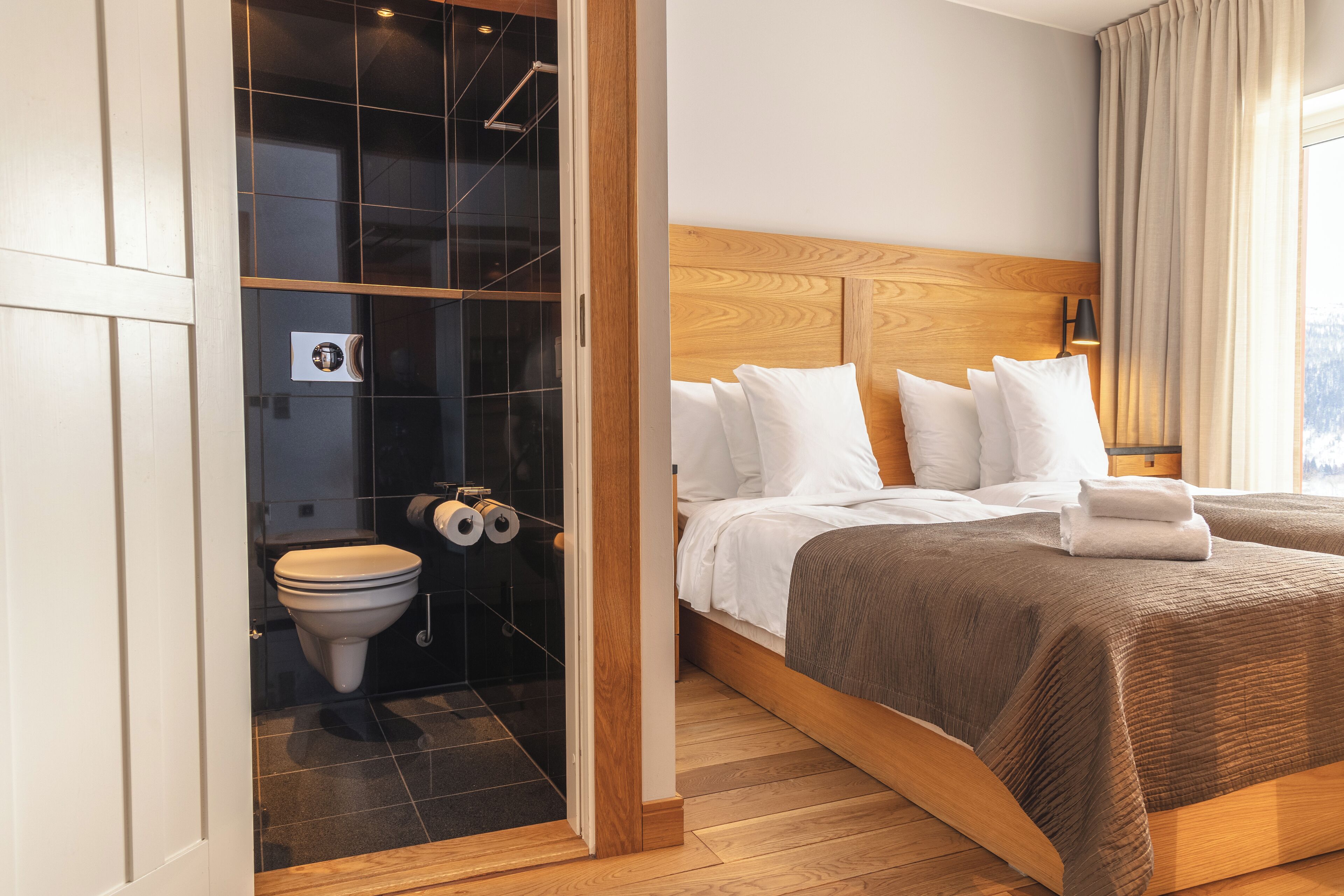 Ein Hotelzimmer mit einem hölzernen Kopfteil, einem großen Bett mit weißer Bettwäsche, Holzboden und einer Duschkabine aus Glas.