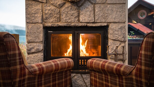 Una chimenea de piedra con fuego, flanqueada por dos sillones a cuadros.