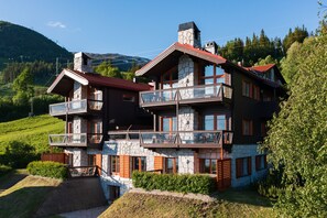 A multi-story chalet with a stone facade, balconies, and a view of the surrounding hills.