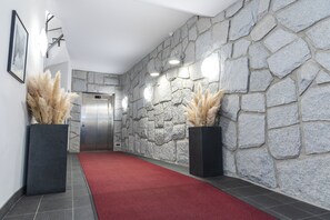 A hallway with a red carpet, stone wall, and an elevator.