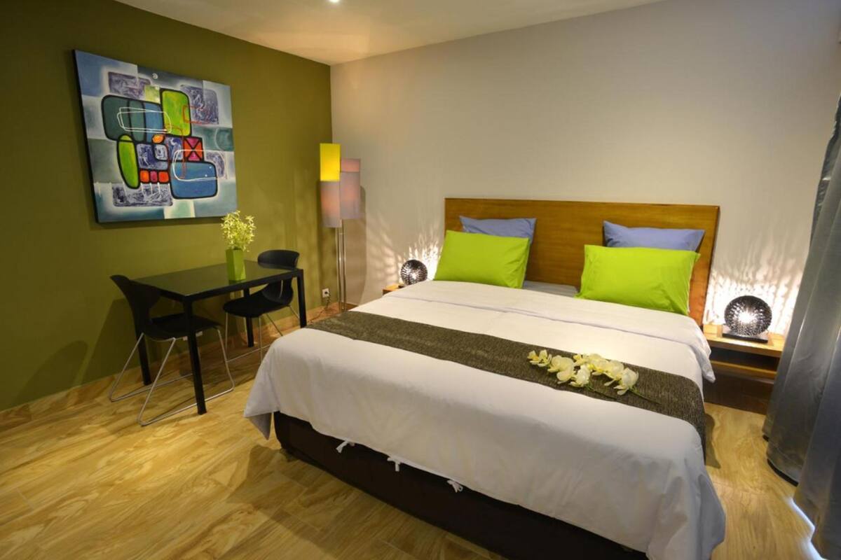 A hotel room with a bed, a desk, a chair, a lamp, and a painting on the wall.