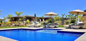 A swimming pool with lounge chairs and umbrellas, surrounded by landscaped gardens and a building with a sloped roof. - Eden Appartel Koné (Kone)