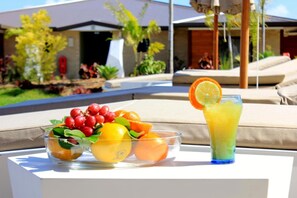 A table with a fruit bowl and a glass of juice on a balcony with a view of a pool and a building. - Eden Appartel Koné (Kone)