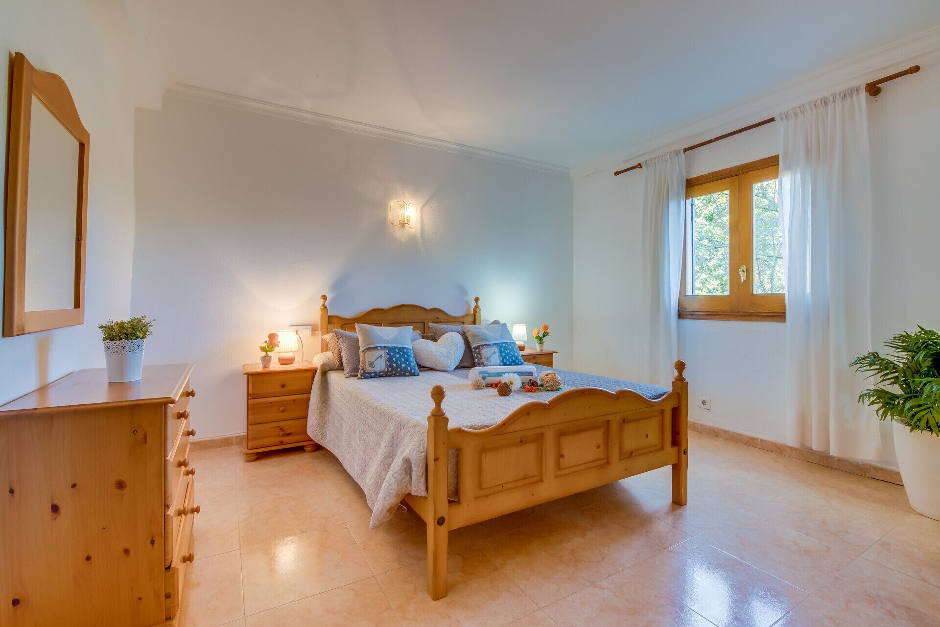 Una camera da letto con un letto di legno, comodini, una cassettiera, uno specchio e una finestra con tende.