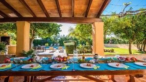 An outdoor dining area with a long table set for a meal, surrounded by greenery and a pool in the background. - Country style Finca Can Verga Pollensa with pool (Pollensa)