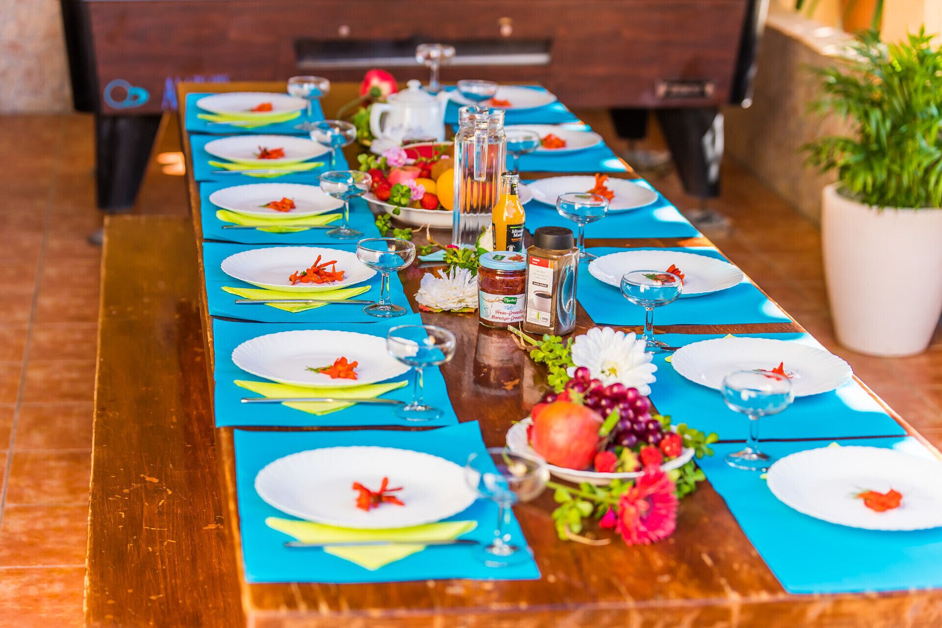 A long dining table set with blue placemats, white plates, and clear glasses.