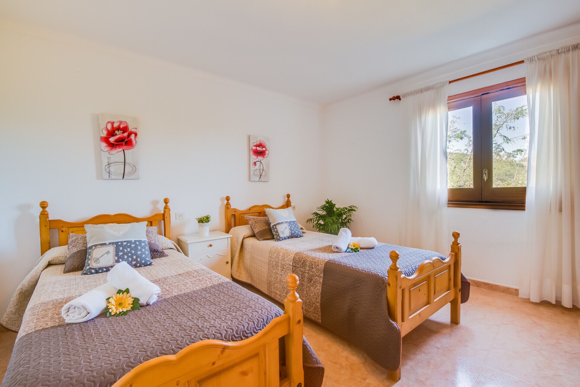A room with two wooden beds, a small bedside table with a plant, and a window with curtains.