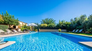 A clear blue swimming pool with lounge chairs and umbrellas, surrounded by greenery and a building with a tiled roof. - Country style Finca Can Verga Pollensa with pool (Pollensa)
