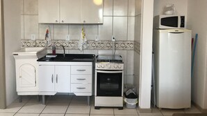 A kitchen with white cabinets, a stove, a microwave, and a refrigerator. - Lagoa Apartments (Florianópolis)