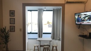 A living room with a TV, a table with stools, a sofa, and a window with curtains. - Lagoa Apartments (Florianópolis)