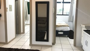 A hotel room with a bed, a dresser, a mirror, and a view of the outside through a window. - Lagoa Apartments (Florianópolis)