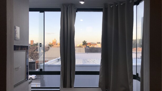 A room with a large window, a table, and a view of a cityscape. - Lagoa Apartments (Florianópolis)