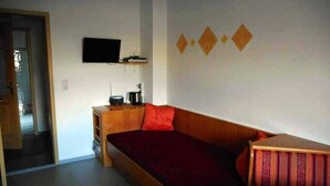 Een kamer met een houten bed, een aan de muur bevestigde televisie en een klein tafeltje met een waterkoker.