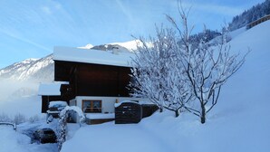 Een houten hut met een ruim terras, omgeven door met sneeuw bedekte bomen en bergen.