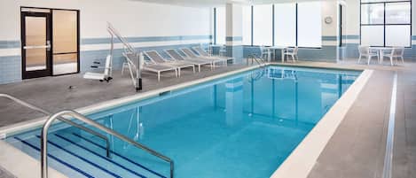 A swimming pool with clear blue water, surrounded by lounge chairs and a tiled floor.