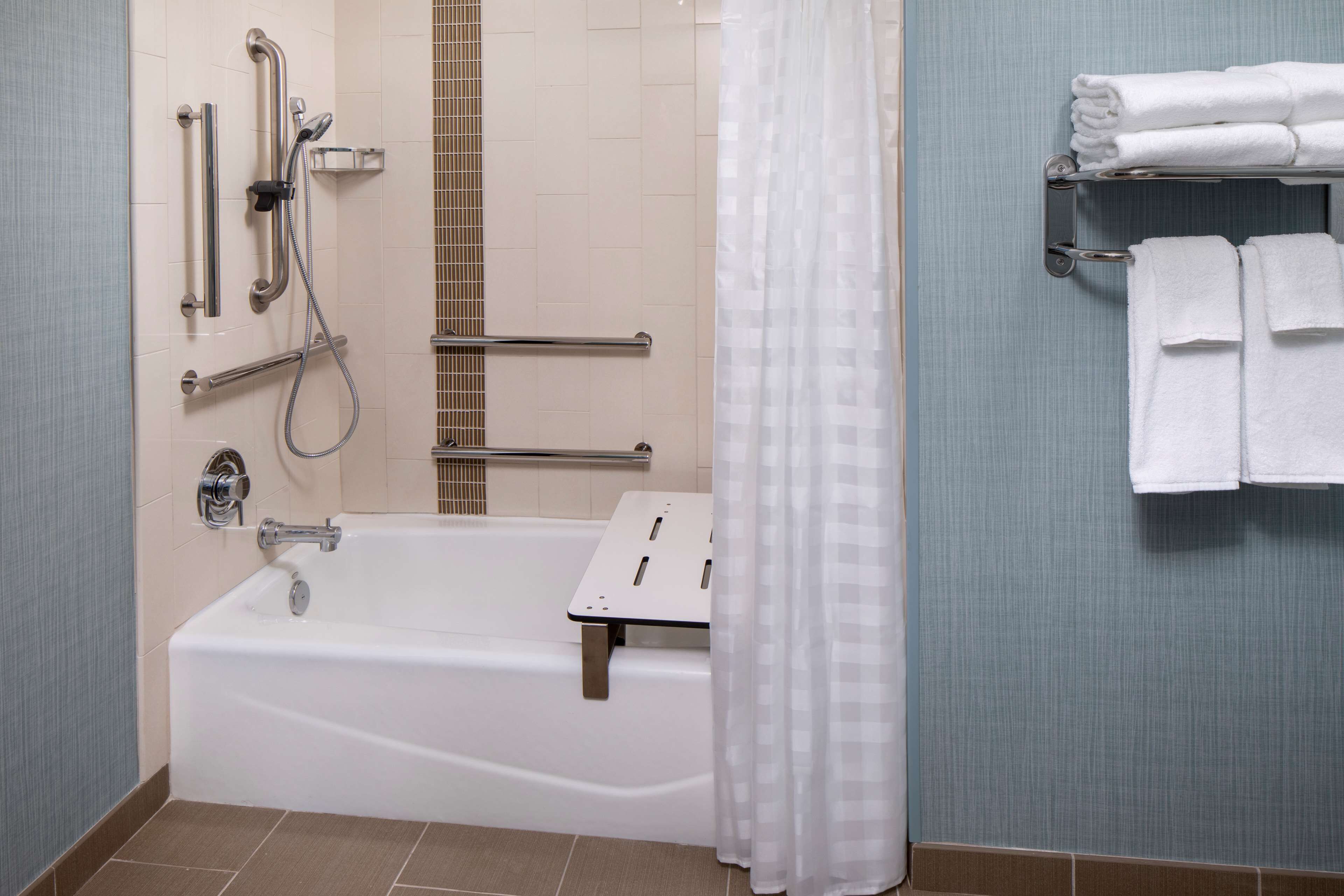 Un baño con bañera, barras de apoyo, panel de control de ducha y toallero con toallas dobladas.