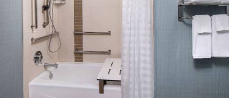 A bathroom with a bathtub, grab bars, a shower control panel, and a towel rack with folded towels.