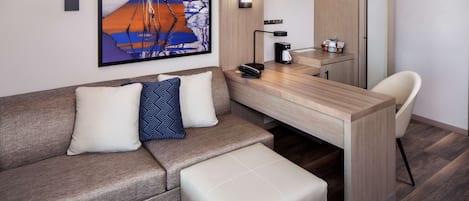 A modern hotel room with a sofa, a small table, a chair, a desk, and a refrigerator.