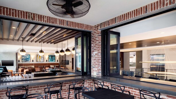 A modern restaurant with brick walls, black furniture, and pendant lighting. - Hyatt Place Mount Pleasant Towne Centre (Mount Pleasant)