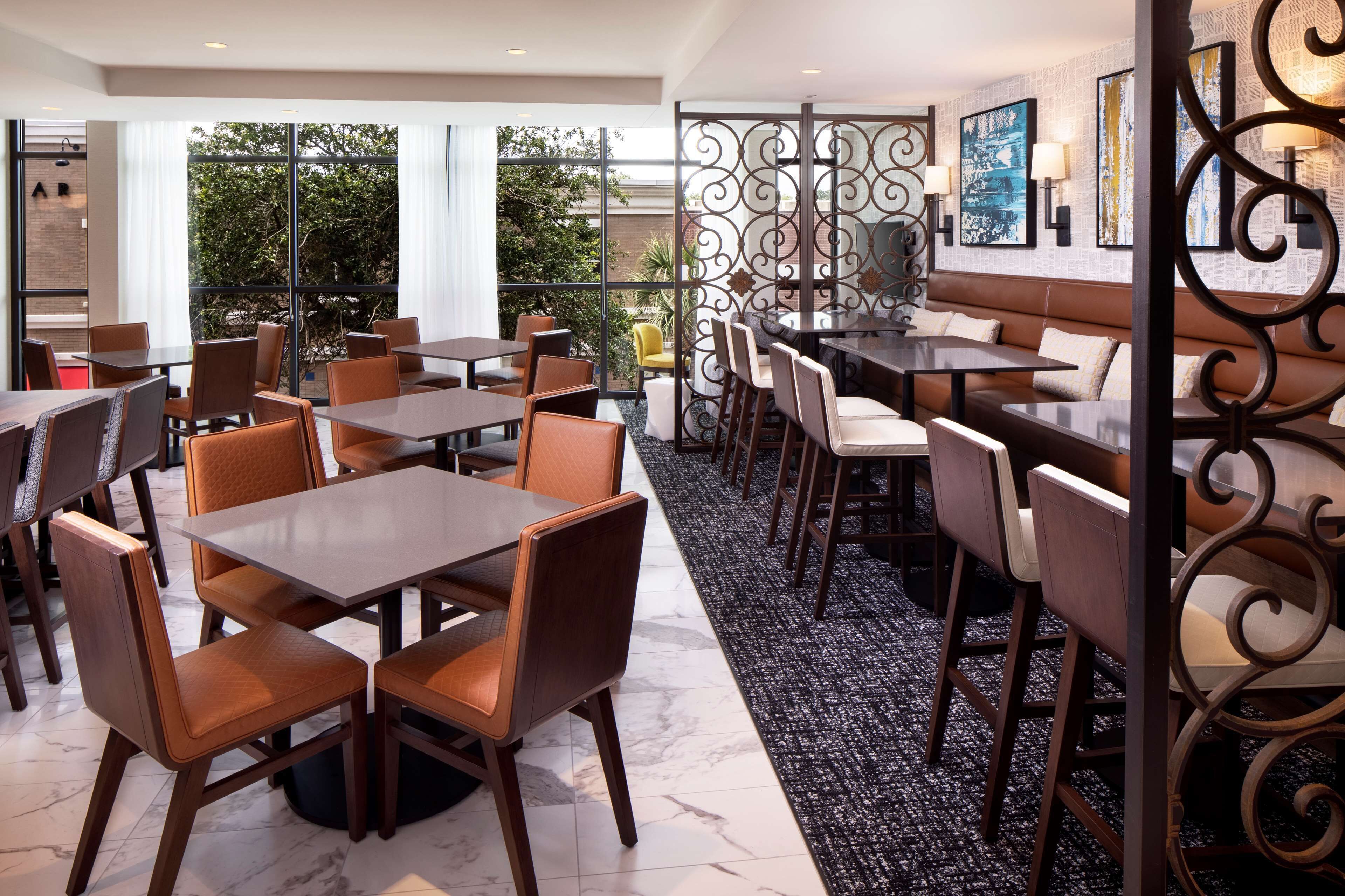 A modern dining area with multiple tables and chairs, a decorative partition, and a view of greenery outside.