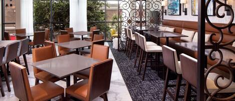Un moderno comedor con varias mesas y sillas, un separador decorativo y vistas al exterior con vegetación.