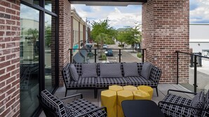 A balcony with a black and white patterned sofa, yellow ottomans, and a small table. - Hyatt Place Mount Pleasant Towne Centre (Mount Pleasant)