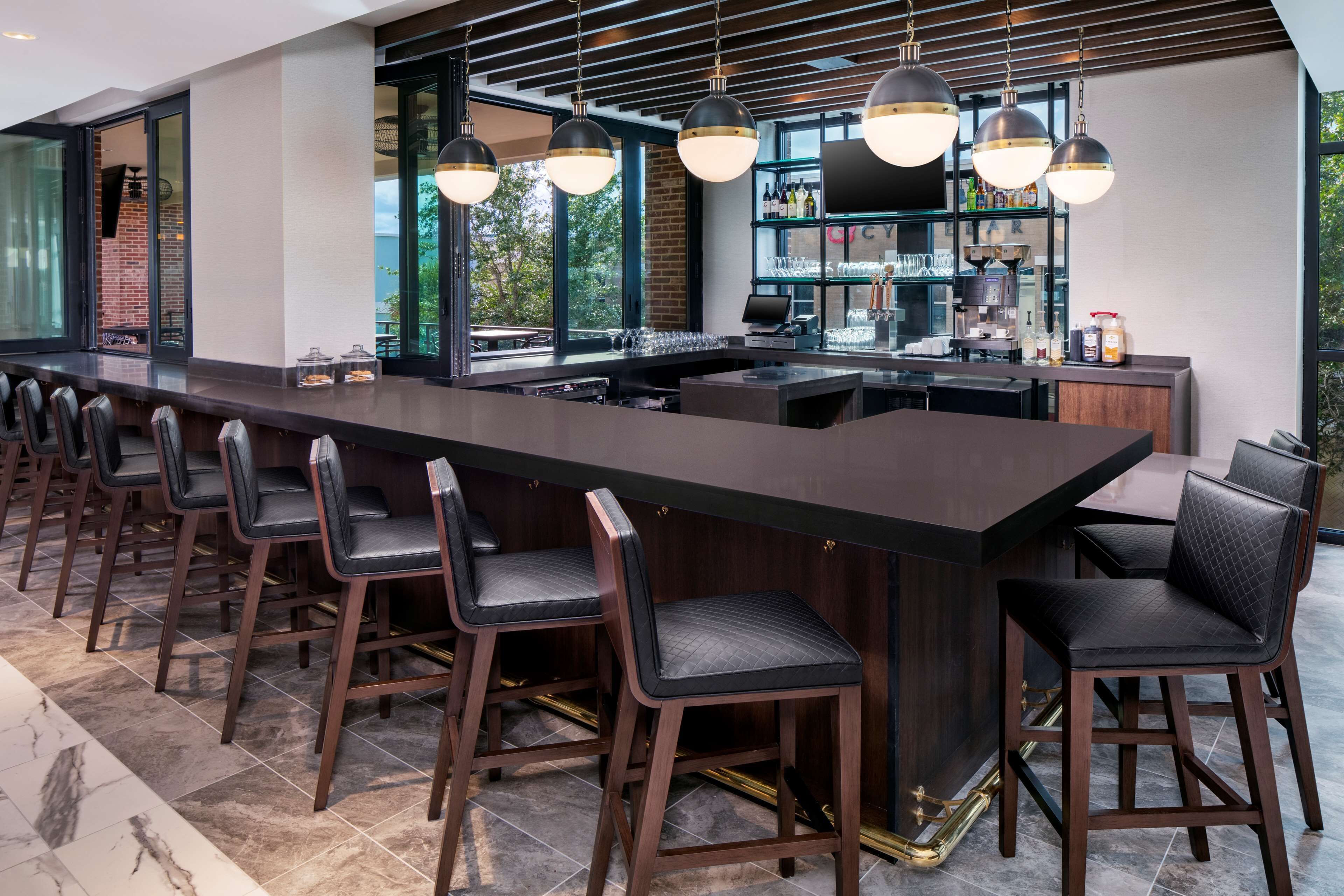 A modern bar area with a long counter, multiple bar stools, and pendant lighting.