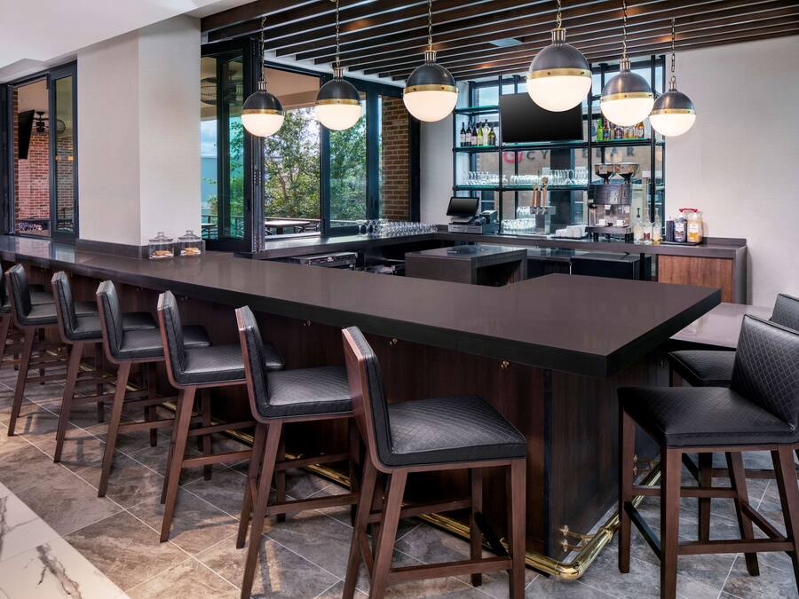 A modern bar area with a long counter, multiple bar stools, and pendant lighting.