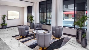 A modern hotel lobby with a marble floor, grey upholstered chairs, a small table, and large windows with curtains. - Hyatt Place Mount Pleasant Towne Centre (Mount Pleasant)