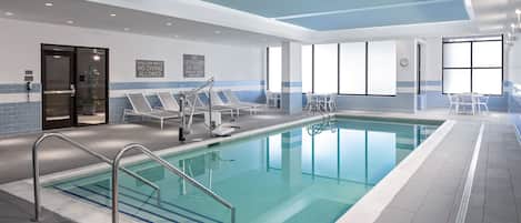Una piscina interior con agua cristalina, barandales de metal y sillas de descanso.