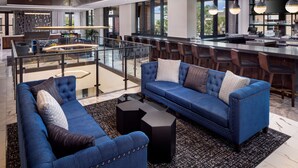 A spacious living area with a blue sofa set, a glass railing, and a modern kitchen in the background. - Hyatt Place Mount Pleasant Towne Centre (Mount Pleasant)