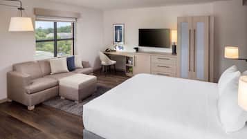 Una habitación de hotel con una cama grande, un sofá, un escritorio con ordenador, un televisor y un armario.