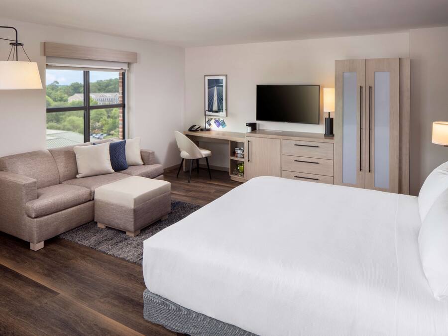 Una habitación de hotel con una cama grande, un sofá, un escritorio con ordenador, un televisor y un armario.