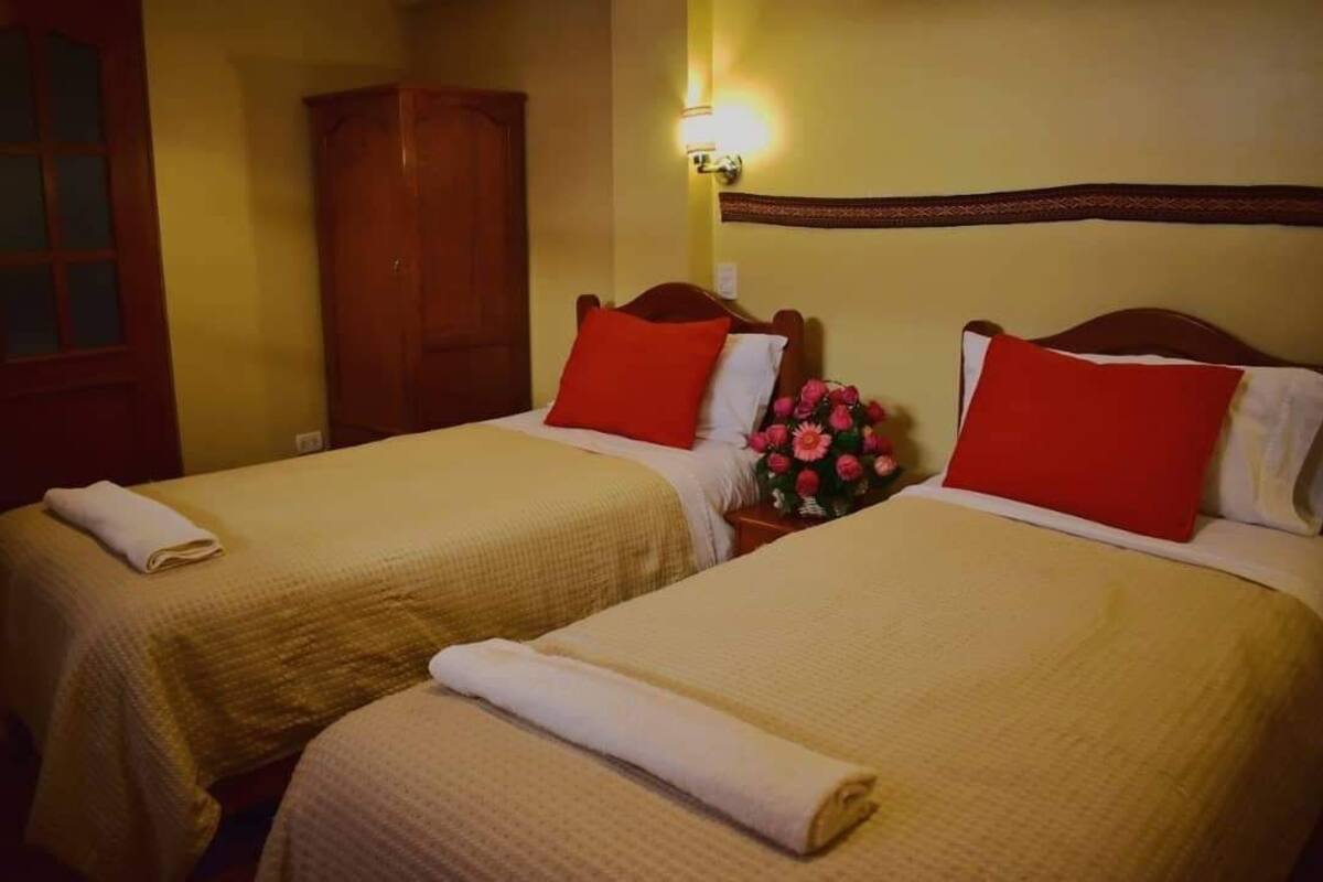 Dos camas individuales con almohadas rojas y blancas, un armario de madera y un aplique de pared.